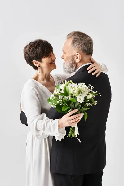 A middle-aged bride and groom in wedding gowns embracing each other, celebrating their special day in a studio setting. — Stock Photo
