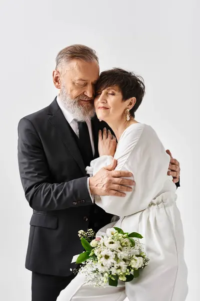 A middle-aged man in a suit lovingly hugs a woman in a white dress, celebrating their special day in a studio setting. — Stock Photo
