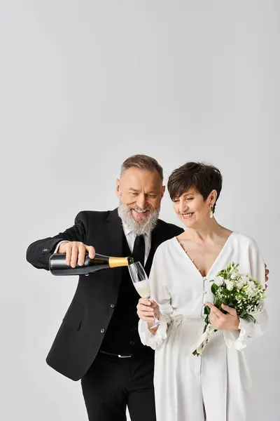 Middle aged bride and groom in wedding attire holding a bottle of champagne, celebrating their special day in a studio setting. — Stock Photo