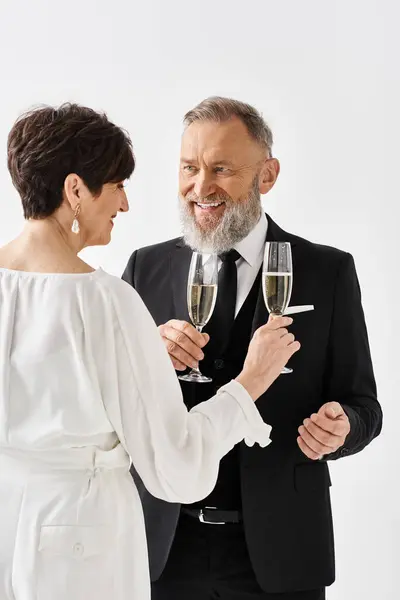 Sposi di mezza età in abiti da sposa che celebrano il loro giorno speciale sollevando flauti di champagne in un ambiente di studio. — Foto stock