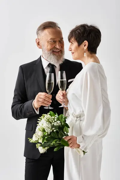 Mariée d'âge moyen et marié en tenue de mariage debout près, tenant des verres de champagne dans un geste de célébration. — Photo de stock