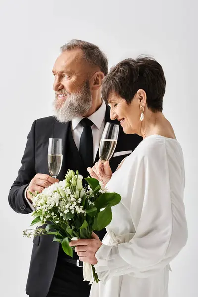 Gli sposi di mezza età in abiti da sposa stanno fianco a fianco, tenendo bicchieri di champagne, celebrando in un ambiente da studio. — Foto stock