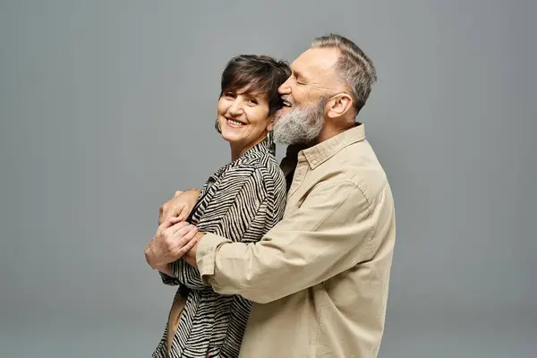 Un hombre y una mujer de mediana edad con un atuendo elegante que comparten un cálido abrazo en un entorno de estudio. - foto de stock