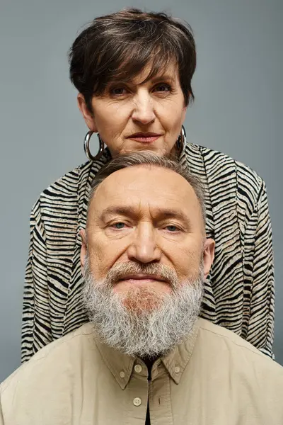 Un hombre barbudo con un atuendo elegante se para delante, mientras una mujer en la espalda mira con una expresión misteriosa. - foto de stock
