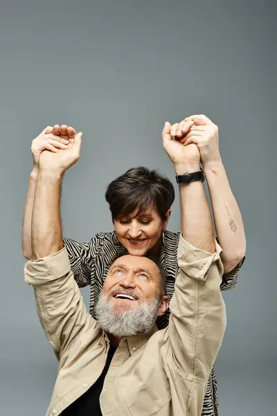 A middle-aged man in stylish attire holds a woman on his shoulders in a studio setting, showcasing strength and affection. — Stock Photo
