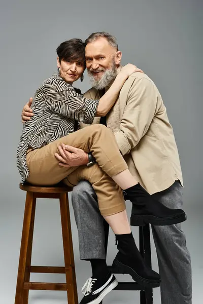 Hombre y mujer de mediana edad con un atuendo elegante sentados en un taburete en un entorno de estudio. - foto de stock