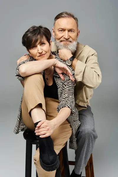 Middle aged man and woman in fashionable attire sitting atop a stool in a studio setting. — Stock Photo