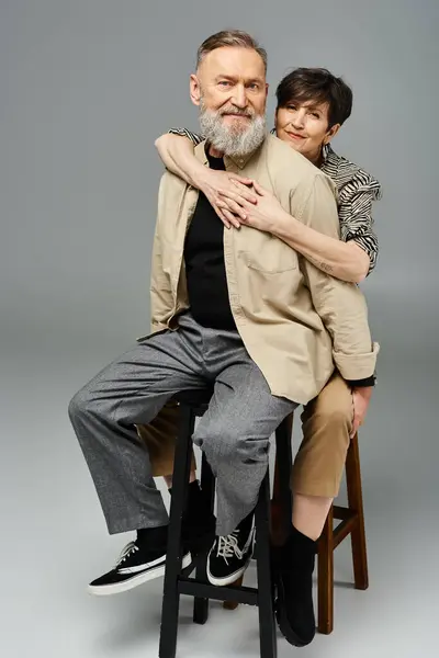 Un hombre y una mujer de mediana edad vestidos con estilo sentados en una silla de madera, disfrutando de un momento juntos en un entorno de estudio. - foto de stock