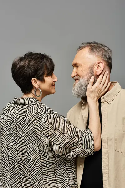 Un hombre y una mujer de mediana edad con un atuendo elegante se paran elegantemente uno al lado del otro en un entorno de estudio. - foto de stock