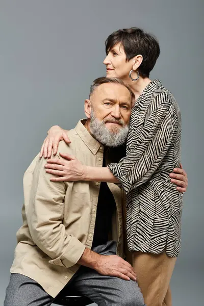 Un hombre y una mujer de mediana edad, vestidos con un atuendo elegante, comparten un abrazo tierno en un entorno de estudio, mostrando amor y conexión. - foto de stock