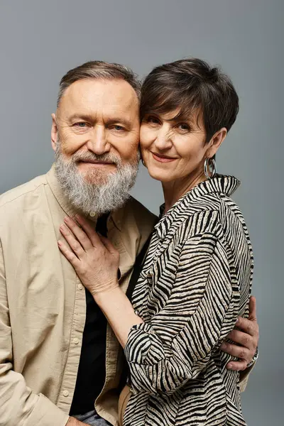 Un hombre y una mujer de mediana edad, vestidos con estilo, comparten un cálido abrazo en un entorno de estudio. - foto de stock