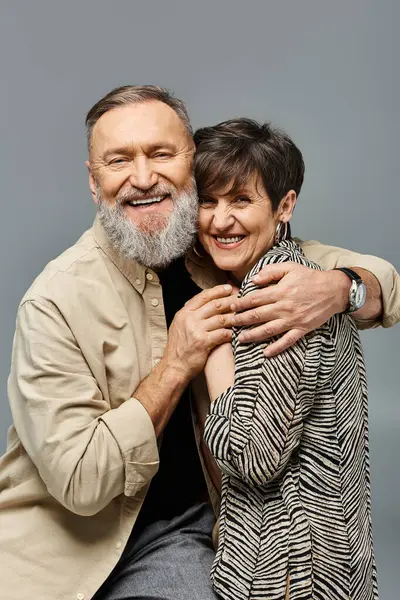 Un hombre y una mujer de mediana edad con un atuendo elegante comparten un abrazo sincero en un entorno de estudio, irradiando amor y conexión. - foto de stock