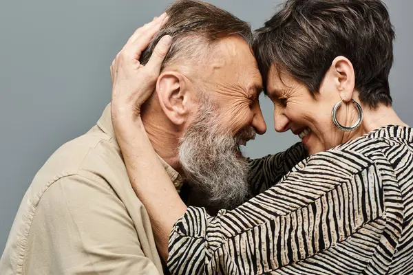 Un hombre y una mujer de mediana edad con un atuendo elegante abrazándose íntimamente en un entorno de estudio. - foto de stock