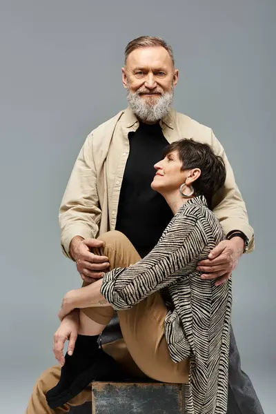A middle-aged man sits triumphantly on top of a woman in stylish attire in a studio setting. — Stock Photo