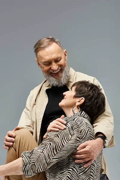 Un hombre y una mujer de mediana edad con un atuendo elegante que comparten un cálido abrazo en un entorno de estudio. - foto de stock