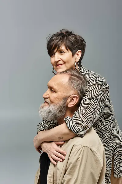 Un hombre de mediana edad lleva galantemente a una mujer en su espalda en un elegante ambiente de estudio. - foto de stock