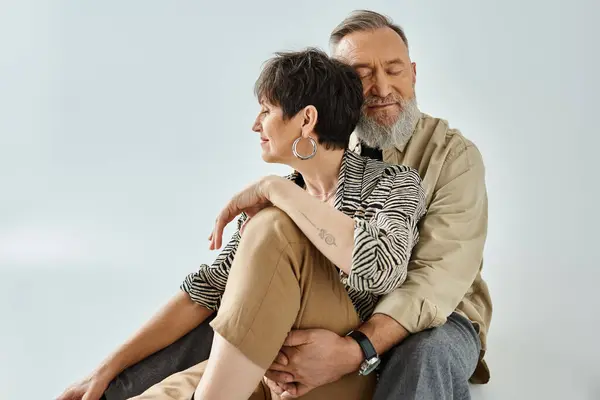 Ein Mann mittleren Alters und eine Frau in stilvoller Kleidung sitzen ineinander verschlungen und schaffen eine optisch eindrucksvolle Komposition in einem Studio-Setting. — Stockfoto