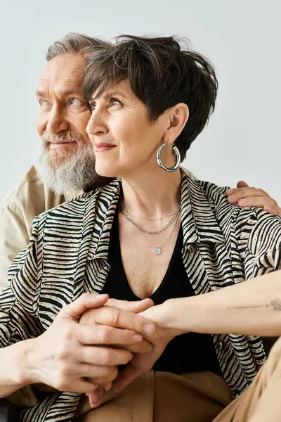 A middle-aged man and woman dressed in stylish attire sit elegantly side by side in a studio setting. — Stock Photo