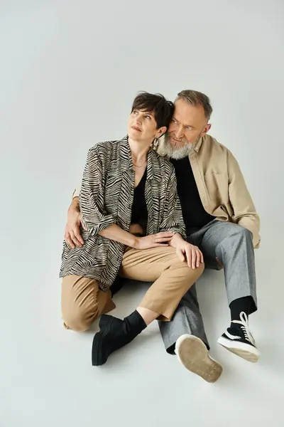 Пара средних лет в стильной одежде сидит рядом друг с другом, излучая элегантность и тепло в студии. — стоковое фото