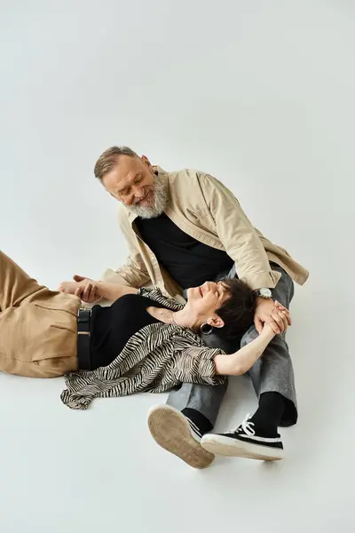 Un couple d'âge moyen en tenue élégante s'assoit les uns sur les autres dans une formation créative de tour humaine dans un cadre de studio. — Photo de stock