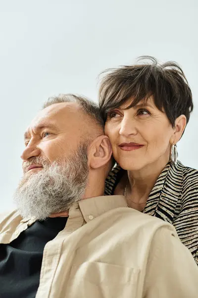 A middle-aged couple in stylish attire sitting closely next to each other, exuding harmony and elegance in a studio setting. — Stock Photo