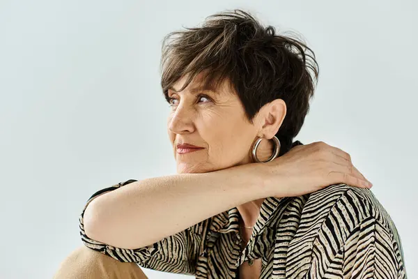 A middle aged woman with short hair sits gracefully on a chair in a studio setting, exuding style and sophistication. — Stock Photo