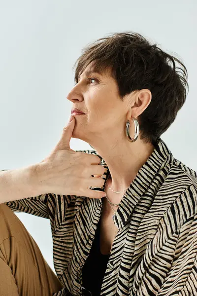 A middle-aged woman with short hair and stylish attire sitting down, deep in thought with her hand on her chin. — Stock Photo