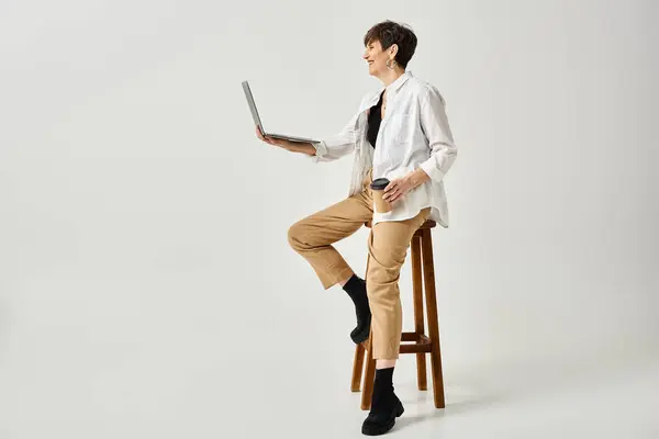 A middle-aged man with short hair is sitting on a stool while holding a laptop in a studio setting. — Stock Photo