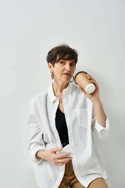 Una mujer de mediana edad con un atuendo elegante se sienta en una silla, sosteniendo una taza con una expresión reflexiva en su cara. — Stock Photo