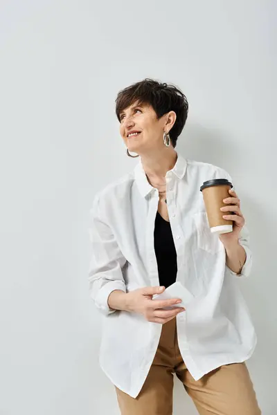 A stylish middle-aged woman with short hair smiles as she holds a cup of coffee in a cozy studio setting. — Stock Photo