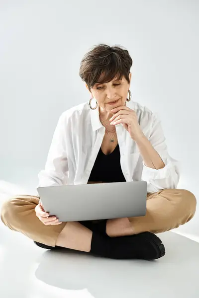 A stylishly dressed middle-aged woman with short hair sits on the floor, focused on a laptop. — Stock Photo