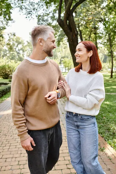 A man and a woman stand side by side on a brick path in a park. — Stock Photo