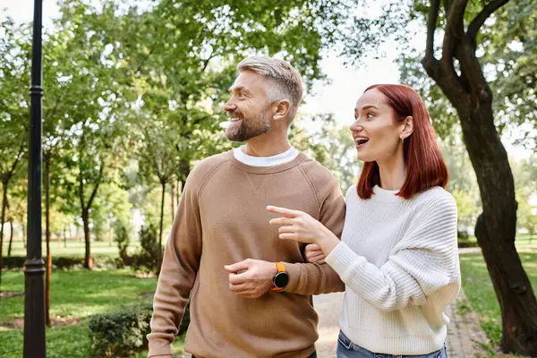 A man and woman leisurely walk through a park, surrounded by greenery. — Stock Photo