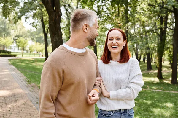 A man and a woman in casual attire stroll through a lush park. — Stock Photo