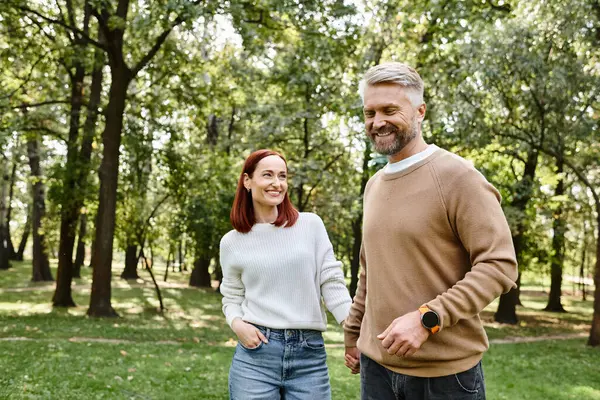 An adult loving couple in casual attire leisurely walking through a park. — Stock Photo