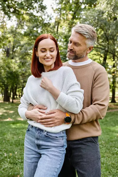 An adult loving couple in casual attire standing in the grassy park. — Stock Photo