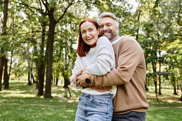 Un uomo e una donna condividono un caloroso abbraccio tra i sereni dintorni di un parco. — Foto stock