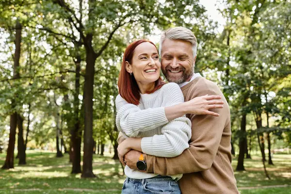 An adult man and woman in casual clothing hug affectionately in a park. — Stock Photo