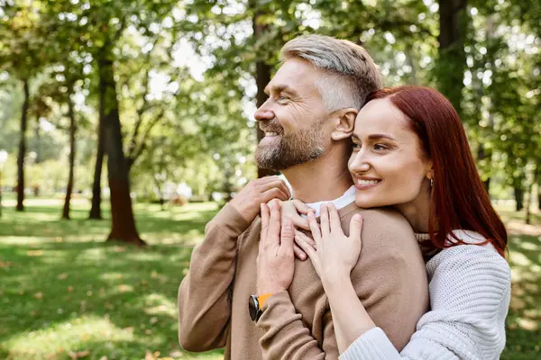 A man tenderly holds a woman in a park, surrounded by greenery and tranquility. — Stock Photo