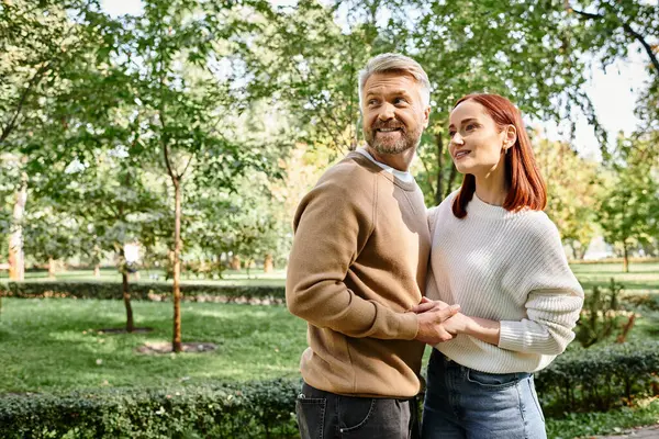 A couple in casual clothing stands together in a park, enjoying a leisurely stroll. — Stock Photo