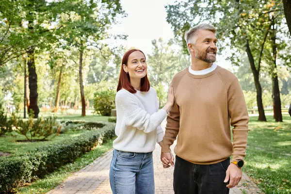 Un hombre y una mujer, una pareja amorosa, caminan casualmente por el parque. - foto de stock