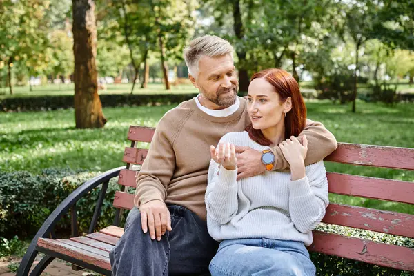 A man and woman in casual attire sit together on a park bench, enjoying each others company. — Stock Photo
