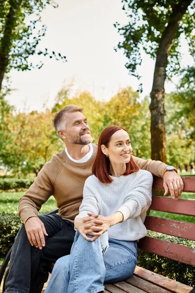 Un homme et une femme en tenue décontractée s'assoient sur un banc de parc, profitant mutuellement de la compagnie. — Photo de stock