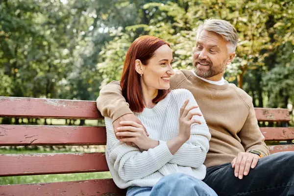 Un couple adulte aimant en tenue décontractée assis ensemble sur un banc de parc. — Photo de stock