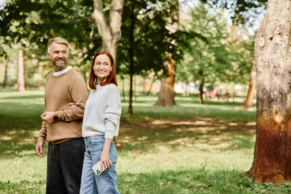 Un uomo e una donna in abbigliamento casual stanno fianco a fianco in un parco lussureggiante. — Foto stock