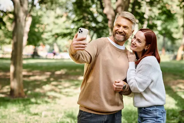 A man and woman capture a moment together in a park by taking a selfie. — Stock Photo