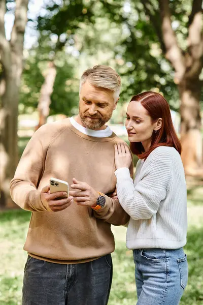 Un hombre y una mujer con ropa casual de pie juntos, la mujer sosteniendo un teléfono celular. - foto de stock