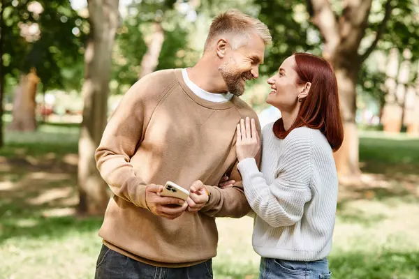 Ein Mann und eine Frau in legerer Kleidung umarmen sich, während sie gemeinsam in einem lebhaften Park stehen. — Stockfoto