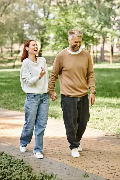 Un hombre y una mujer pasean por una acera con atuendo casual. - foto de stock