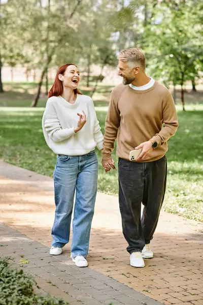 A man and woman in casual attire walk together on a sidewalk in a park. — Stock Photo